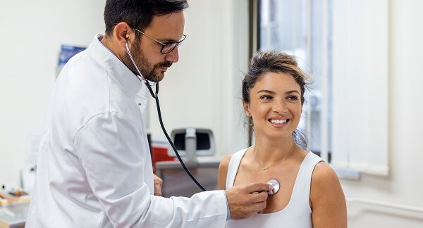 mejores cardiólogos - Uno de los mejores cardiólogos en México escuchando con un estetoscopio el ritmo cardiaco de una mujer joven