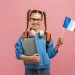 de las mejores escuelas de francés, una estudiante con coletas sostiene una laptop en una mano y en la otra una bandera de francia