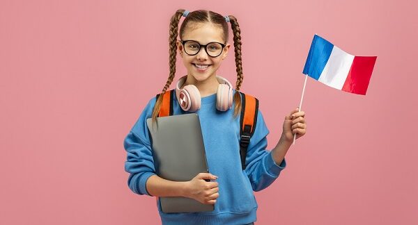 de las mejores escuelas de francés, una estudiante con coletas sostiene una laptop en una mano y en la otra una bandera de francia