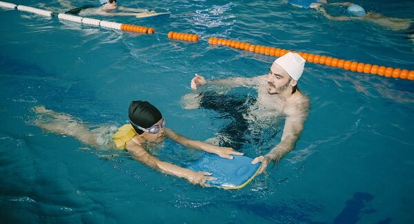 escuelas de natación - un instructor enseña a un niño a nadar apoyado de una tabla