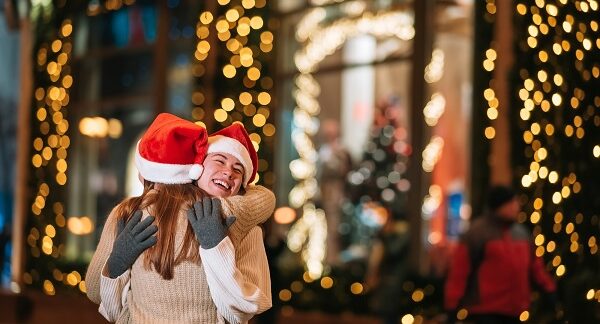 lugares para pasar la Navidad - dos amigas se abrazan en un sitio rodeado de luces navideños
